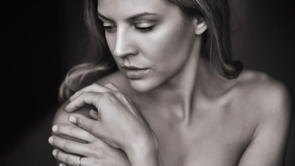 Close-up of a woman with smooth, radiant skin touching her cheek, beside a cream jar and serum bottle.