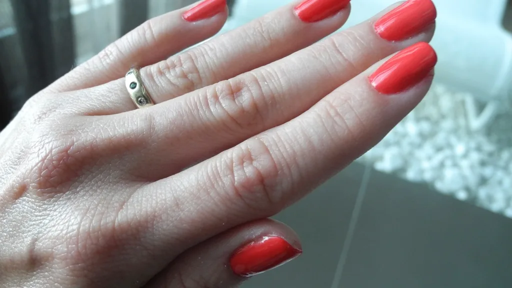 Hands with a glossy gel-effect manicure next to bottles of nail polish.