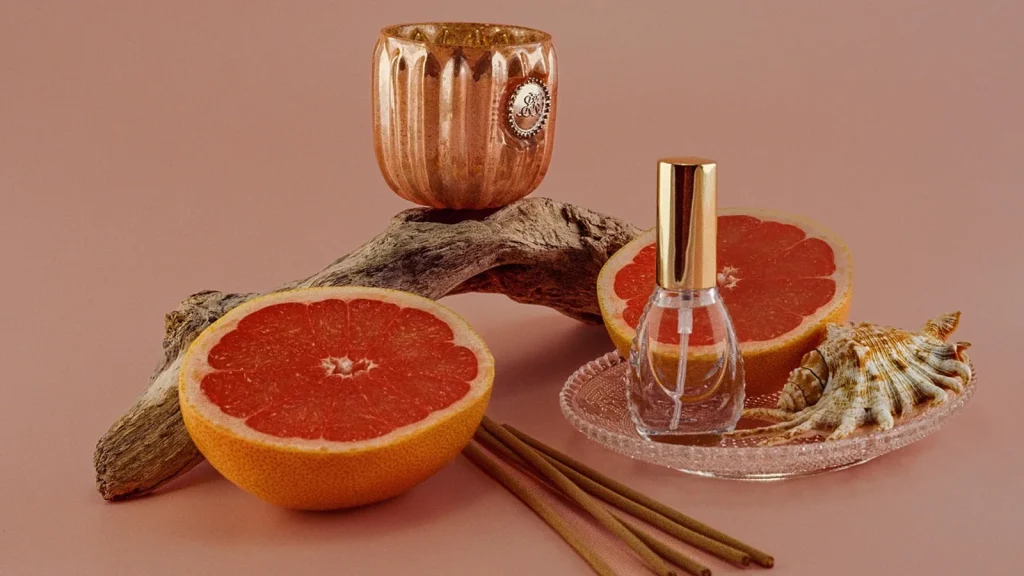 A lit amber jar candle beside a honey dipper and autumn leaves on a wooden table.