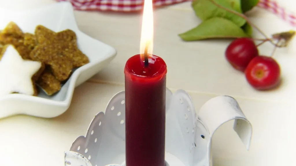 A lit scented candle with iced snowflake cookies and festive decorations.