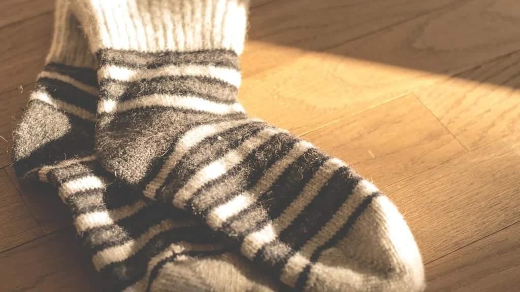 Feet soaking in a warm foot bath with salts, with wool socks nearby in a cozy winter setting.