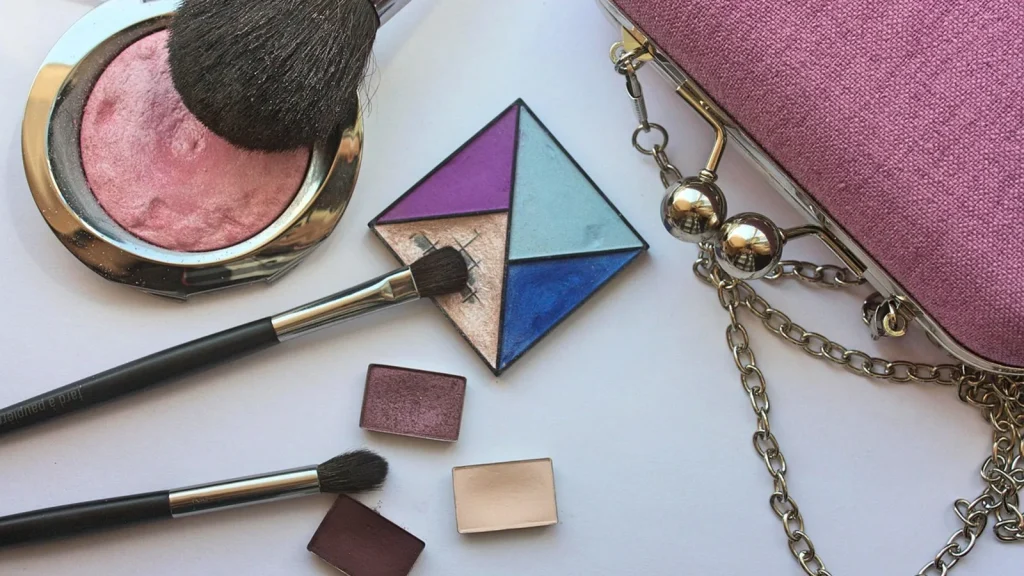 An open small cosmetic bag spilling hand cream, lip balm, compact powder and wipes into a handbag.