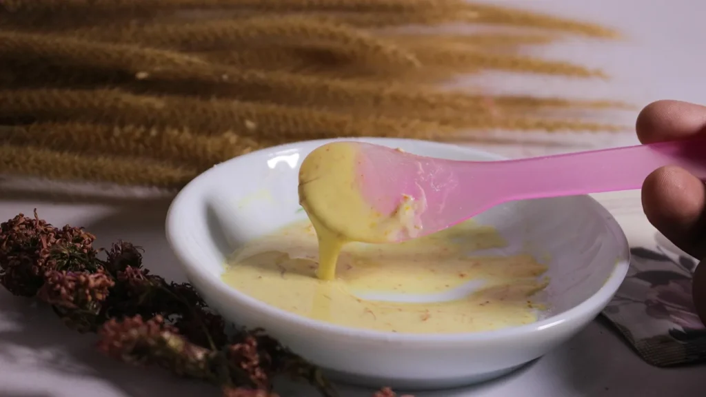 A bowl of homemade hair mask with honey, aloe vera and oil beside a woman's long hair.