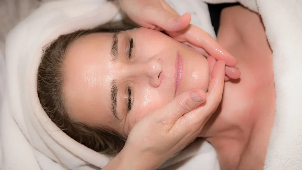 A woman gently using a small electric facial massager on her cheek.