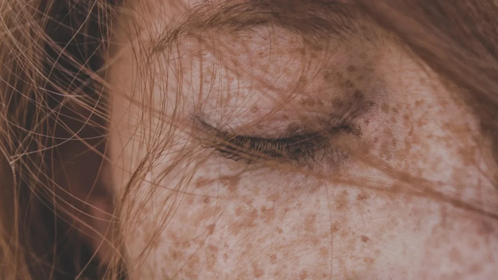 A woman gently massaging a creamy exfoliating peel on her face in front of a bathroom mirror.