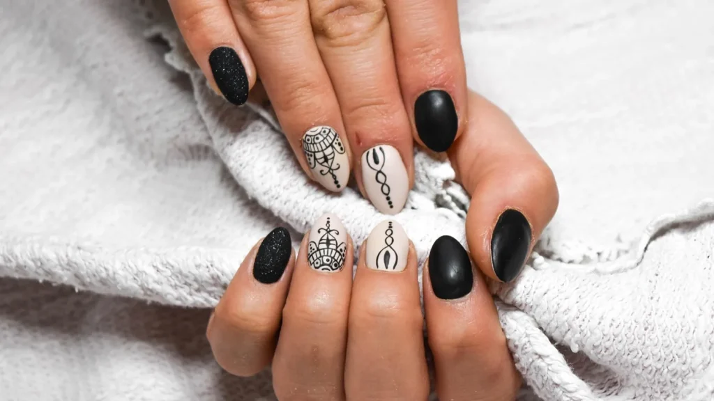 Hands with dark burgundy manicured nails holding a fallen autumn leaf.