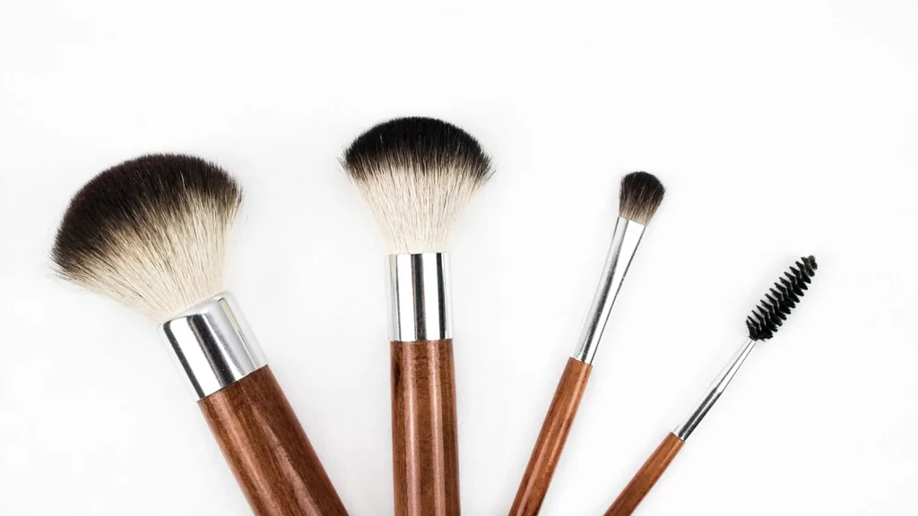 A soft brush dipped in loose mineral powder, with a woman gently dusting powder on her cheeks.