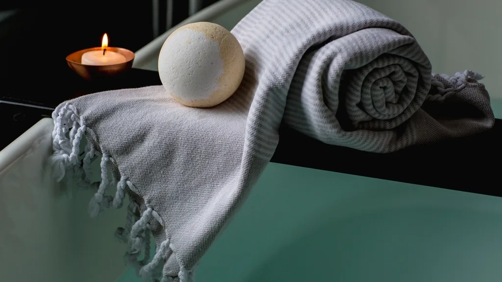 Bath oil being poured into a filled bathtub surrounded by candles and towels.