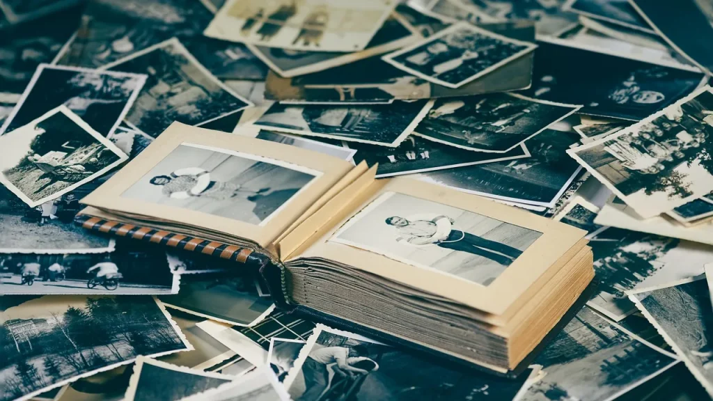Hands arranging printed photos in a photo album with keepsakes around it.