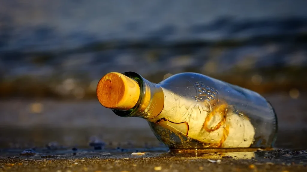 A bottle of tanning oil on a beach towel with sunglasses and sand.