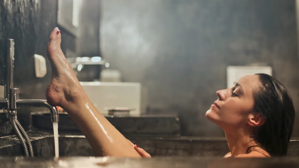 A bottle of shower oil on a shelf in a steamy shower with water running.