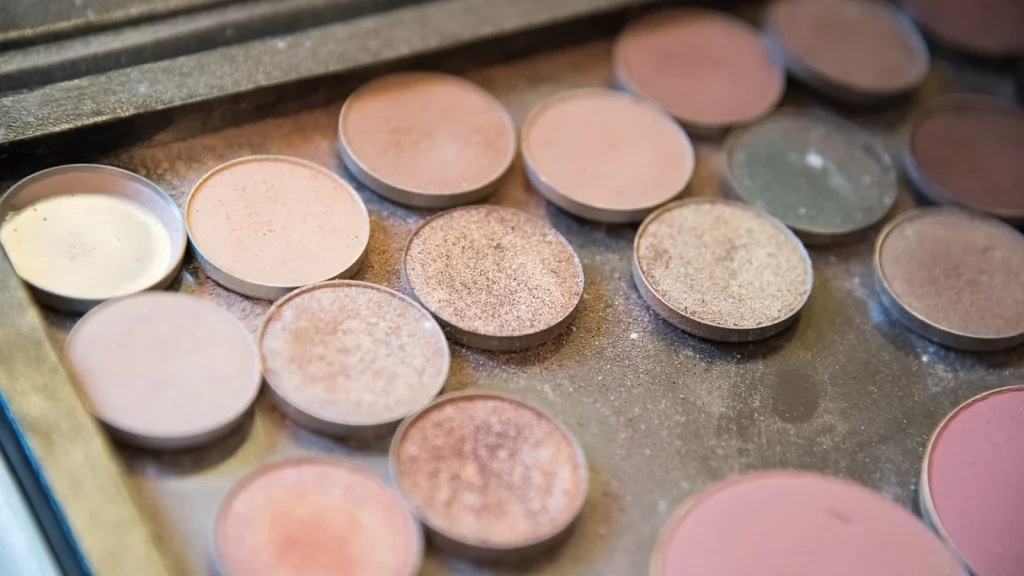 Autumn makeup products, a warm eyeshadow palette, primer and loose powder, laid out with brushes.