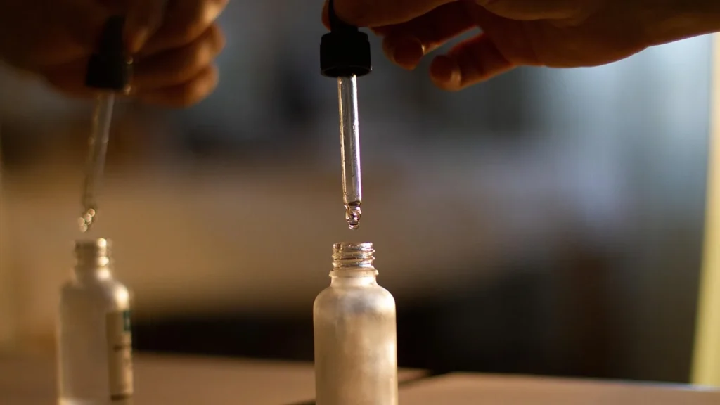A woman applying a few drops of light oil serum to her face and neck from a dropper.