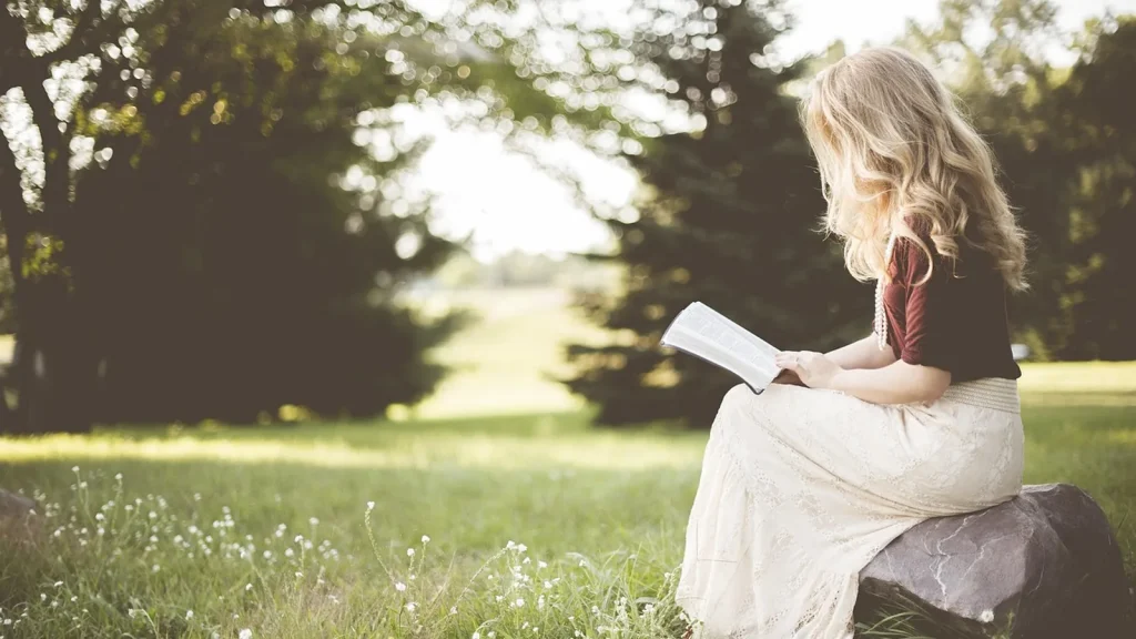 A relaxed woman reading a book with a cup of tea under a blanket on a cozy sofa.