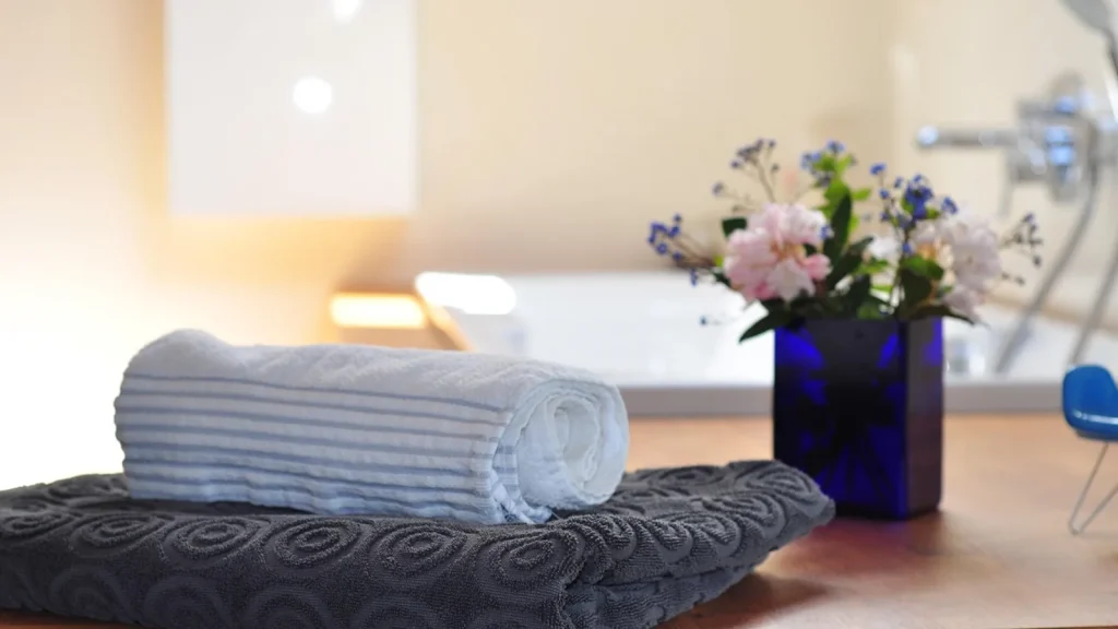 A home spa setup with rolled towels, candles, body scrub and skincare products.