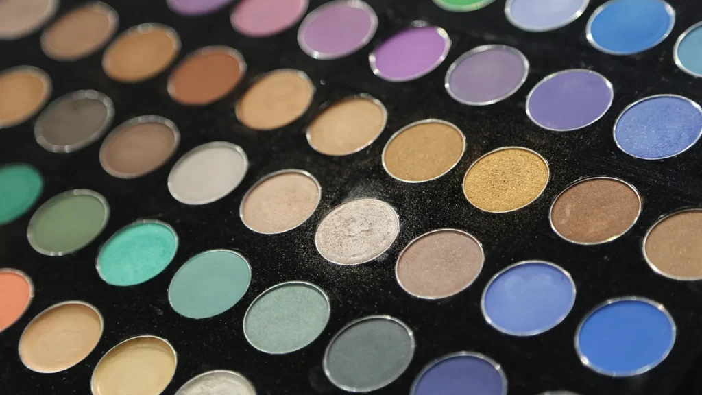 An open colorful eyeshadow palette with matte and shimmer shades and a makeup brush.