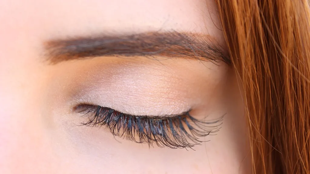 Close-up of a woman filling in her eyebrow with a brow pencil, brow gel and pomade beside.