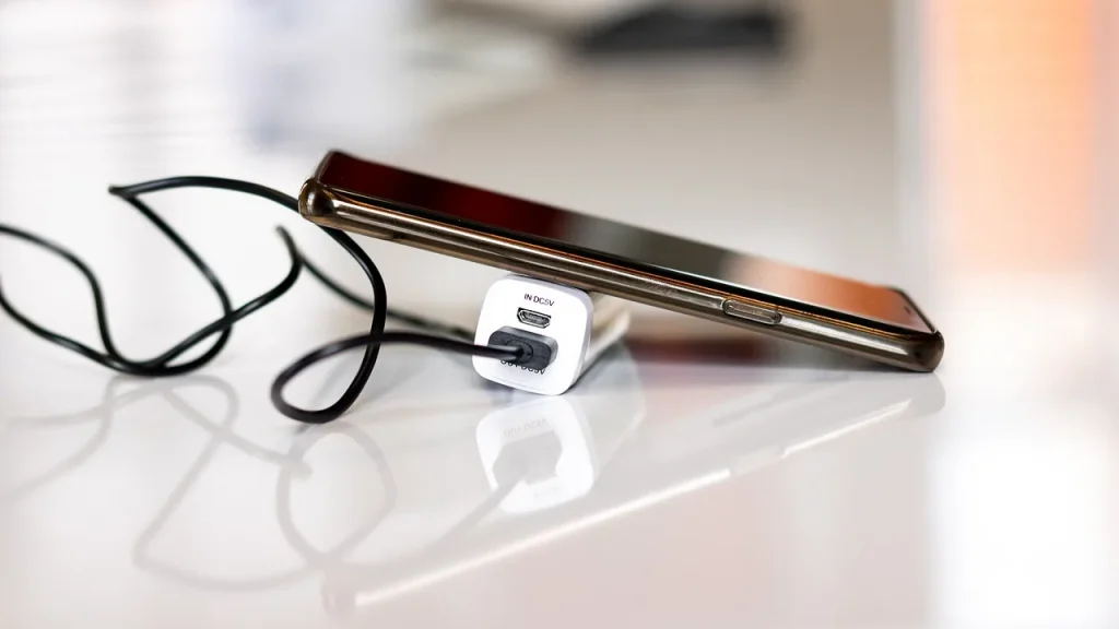 A compact power bank charging a smartphone next to an open handbag.