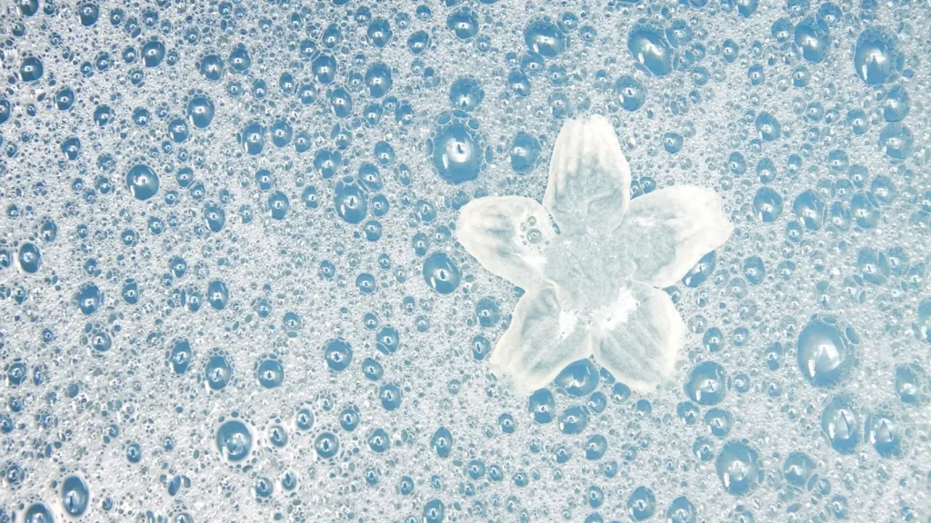 A hand holding thick colorful foam over a bubble-filled bath.