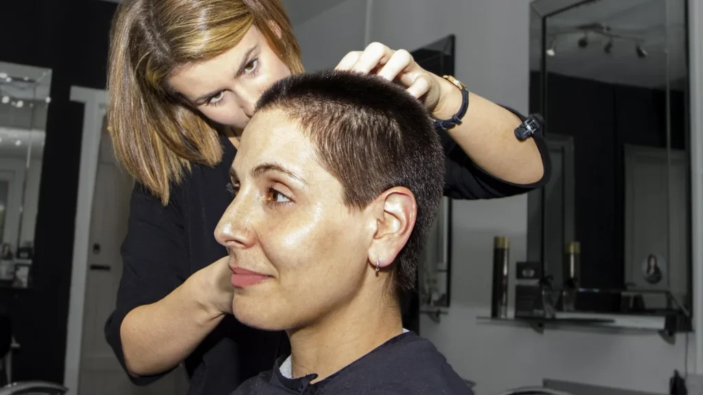 Professional hair care bottles on a salon shelf with a hairdresser treating a client's hair in the background.