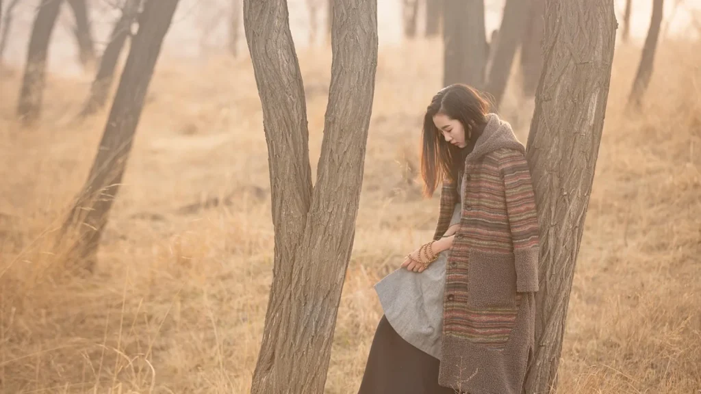 A woman in a cozy knit cardigan walking among autumn leaves.