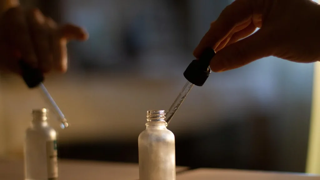 Clear hydrating serum dripping from a glass dropper onto fingertips.