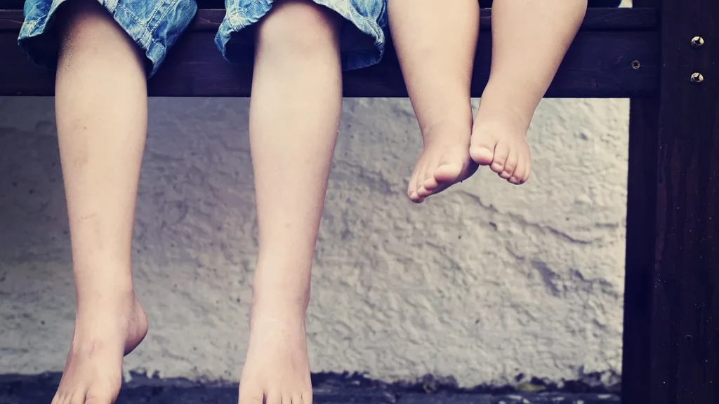 A parent measuring a child's foot against a ruler next to a pair of small sneakers.