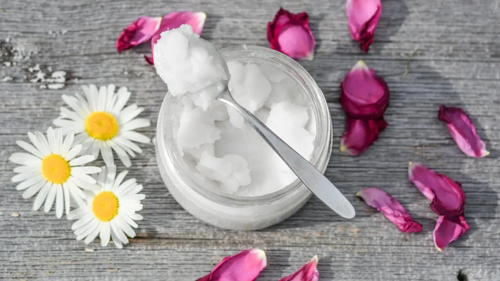 A jar of coconut oil next to a halved coconut, with face skincare beside it.