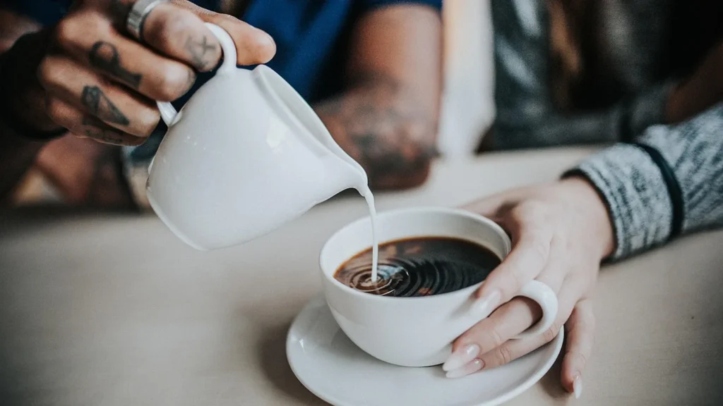 A cup of freshly brewed coffee with coffee beans and a grinder on a morning table.